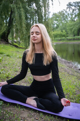 A young, attractive blonde woman meditates in nature, radiating peace and inner harmony.