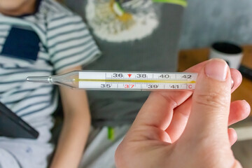 girl holding thermometer in hand, close-up with temperature, bed and sick child in background, cold