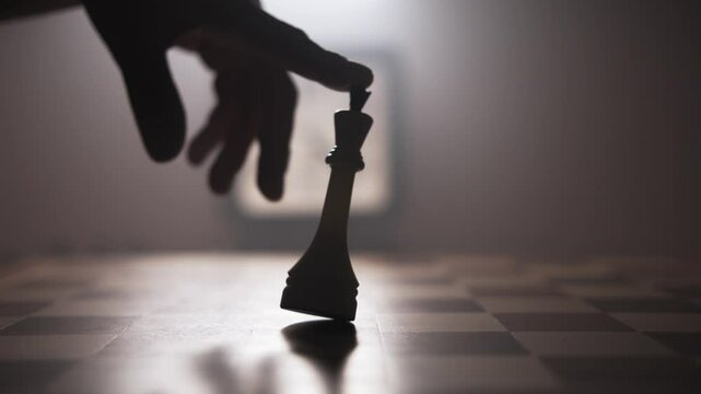 A man swings a chess piece on a board in a circular motion with his index finger