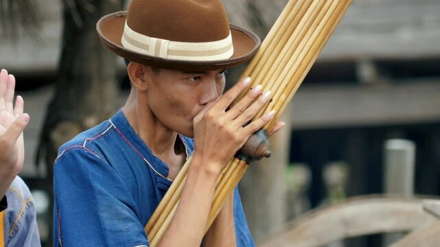 Young Asian man wearing a cowboy hat playing the Khaen, a traditional musical instrument of the Isan region of Thailand. video 4K