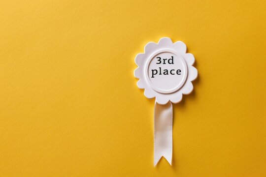 A minimalist studio shot of a third place award rosette on a yellow backdrop