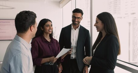 Diverse business team of happy young colleagues talking in boardroom in work break, standing together, discussing teamwork, partnership, successful product release, smiling, laughing - Powered by Adobe