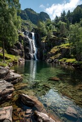 Majestic waterfall cascading over rocks into a serene green pool surrounded by lush trees and magnificent mountains under a clear blue sky