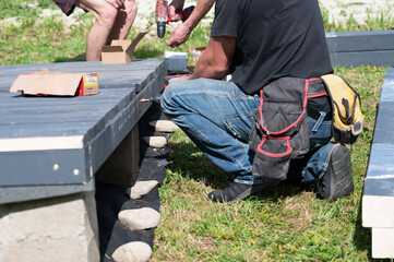 A master carpenter is driving large screws to secure the frame and floor in the gazebo.