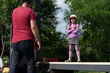 A little girl is talking to a man who is helping to install a gazebo in the garden.