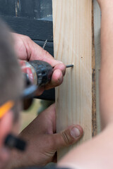 Screwing the board with a screwdriver, installing a wooden gazebo.
