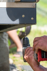 A master carpenter is driving large screws to secure the frame and floor in the gazebo.