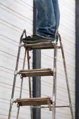 Men's legs standing on a metal ladder with wooden steps.