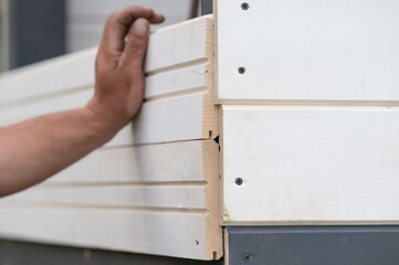 The builder attaches the wall to the gazebo frame using screws and a screwdriver.