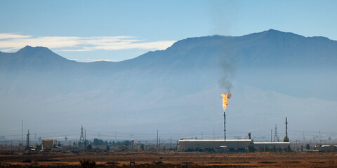 An industrial facility in Iran with a torch burning associated gases, Against the backdrop of...