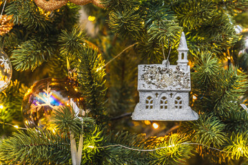 A Christmas tree toy in the form of a fairy-tale house hangs on a sparkling tree. festive background for New Year or Christmas.
