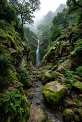 Serene Waterfall Cascading Down Rocky Cliffs Surrounded by Lush Greenery Under Foggy Atmosphere in Tranquil Natural Landscape