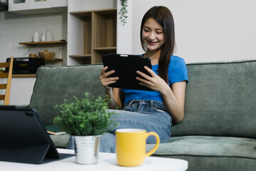 Smiling young Asian woman using digital tablet at home, enjoying remote work or online...