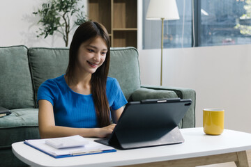 Smiling young Asian woman using digital tablet at home, enjoying remote work or online...