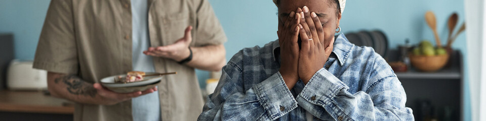 Black woman covering face with hands standing in foreground while Caucasian man gesturing with...