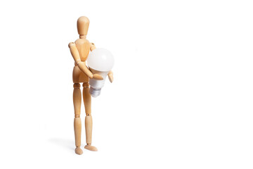 A wooden toy mannequin holding a light bulb in his hands on white background
