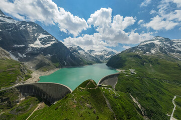 A breathtaking aerial view of a turquoise mountain reservoir surrounded by snow-capped peaks. A...