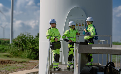 Maintenance engineer team standing at windmills at wind turbine farm. Group of people wear safety...