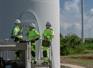 Maintenance engineer team standing at windmills at wind turbine farm. Group of people wear safety...