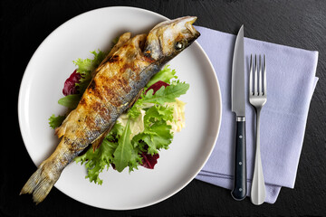Plate with grilled sea bass and green salad with napkin and cutlery