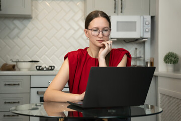 Young woman wearing glasses and a red sleeveless top is sitting at a glass table in a modern...