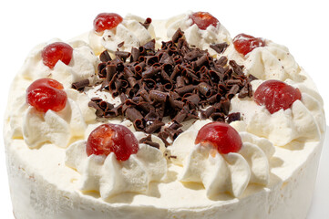 Close-up top view of a Black Forest cake with decorative whipped cream and glossy cherries encircling chocolate curls in the center. The texture looks rich and tempting.