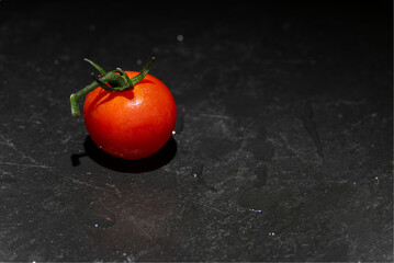 Single Tomato on Black Stone. A single red tomato with water drops lies on a dark stone floor....
