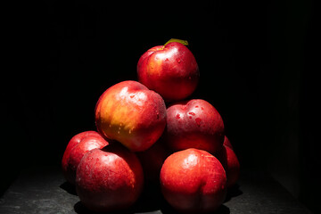 A pyramid of nectarines with water droplets stands out against a dark background. The lighting...