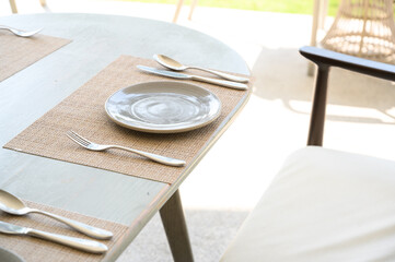 white dish with stainless steel spoon, knife, and fork on plate mat setting on the restaurant outdoor table.