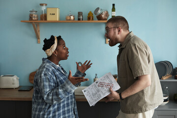 Young adult Black woman gesturing emotionally while arguing with young adult Caucasian man holding...