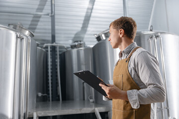 Fototapeta premium Young caucasian male brewer with clipboard in brewery