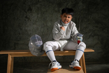 A boy in fencing gear sitting on a bench, ready for the épée competition