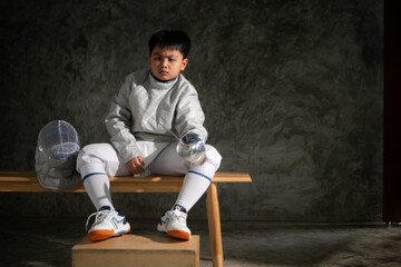 A boy in fencing gear sitting on a bench, ready for the épée competition