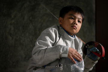 A boy in fencing gear sitting on a bench, ready for the épée competition