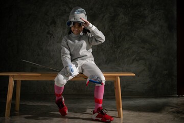 A girl in fencing gear sitting on a bench, ready for the épée competition