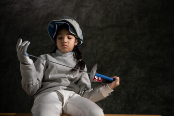A girl in fencing gear sitting on a bench, ready for the épée competition