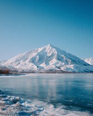 Naklejka premium Snowy mountain peaks and frozen lake under clear blue sky.