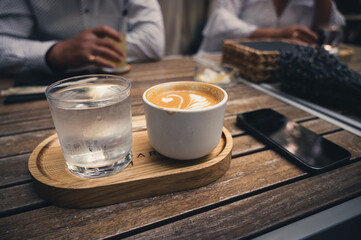 Cup of Cappuccino on a Wooden Table with Phone and Glass of Water Besides It