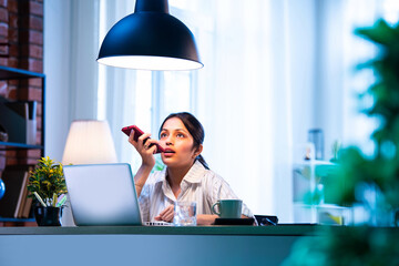 Indian businesswoman multitasking at desk, attending speaker call with cheerful body language