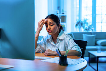 Indian businesswoman feels pressure and headache while working on laptop at modern office desk