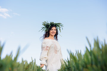 Beautiful Young Woman in Traditional Embroidered Dress and Green Wheat Wreath Looking at Camera in...