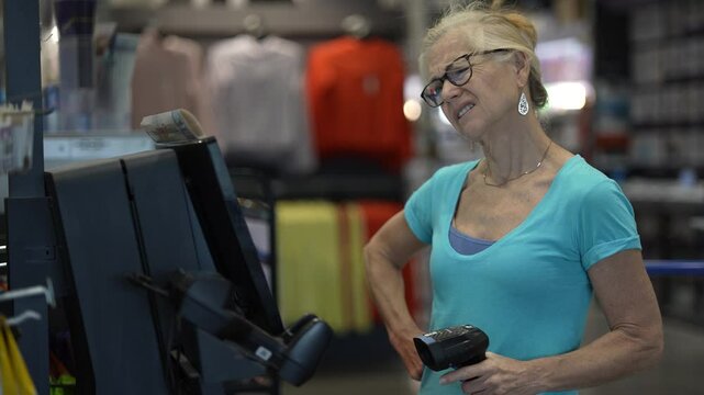 In a hardware store, a frustrated confused mature woman is using a self checkout station, scanning items with a handheld scanner while preparing to complete her purchase.