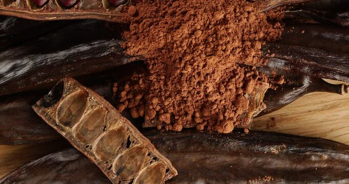 Carob pods and powder on a wooden board, top view, on a rotating table.
