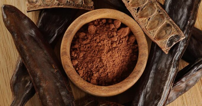 Carob pods and powder on a wooden board, top view, on a rotating table.