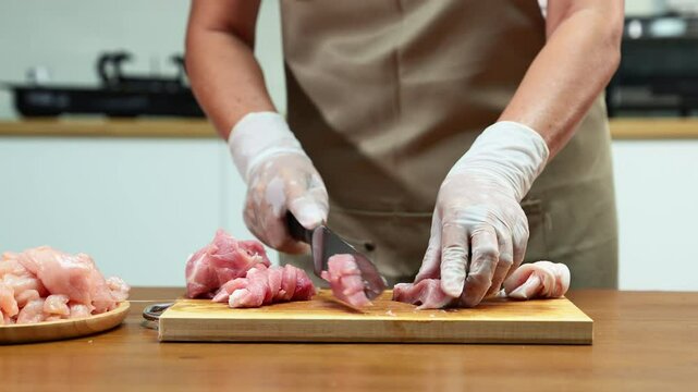 Closeup of a gloved hand slicing raw pork loin on a wooden board in a clean kitchen. Perfect for culinary, food prep