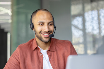 A smiling man wearing a headset appears to be in a customer service or call center environment,...