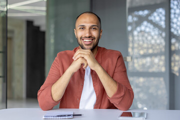 A smiling man with his hands clasped, seated at a table, creating a warm and approachable impression.