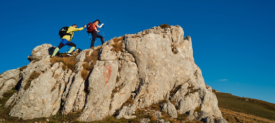 Couple hikers trek up a rocky mountain trail, enjoying a scenic view above the clouds, with...