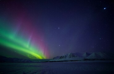  night landscape of the aurora borealis glowing over a snow-covered mountain range, vivid green, purple, and blue light waves dancing across a starry sky, crisp clear atmosphere, high-detail