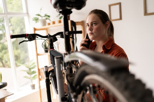 Young woman repairing bicycle at home calling her mechanic for advice using smartphone